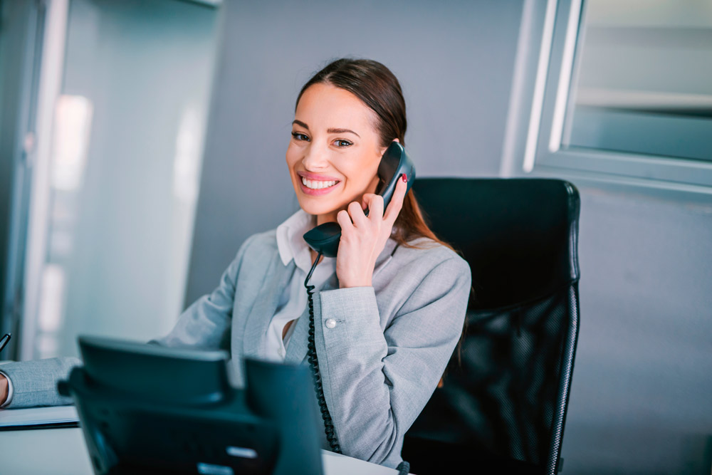 Foto de uma secretária empresarial sorridente falando ao telefone.